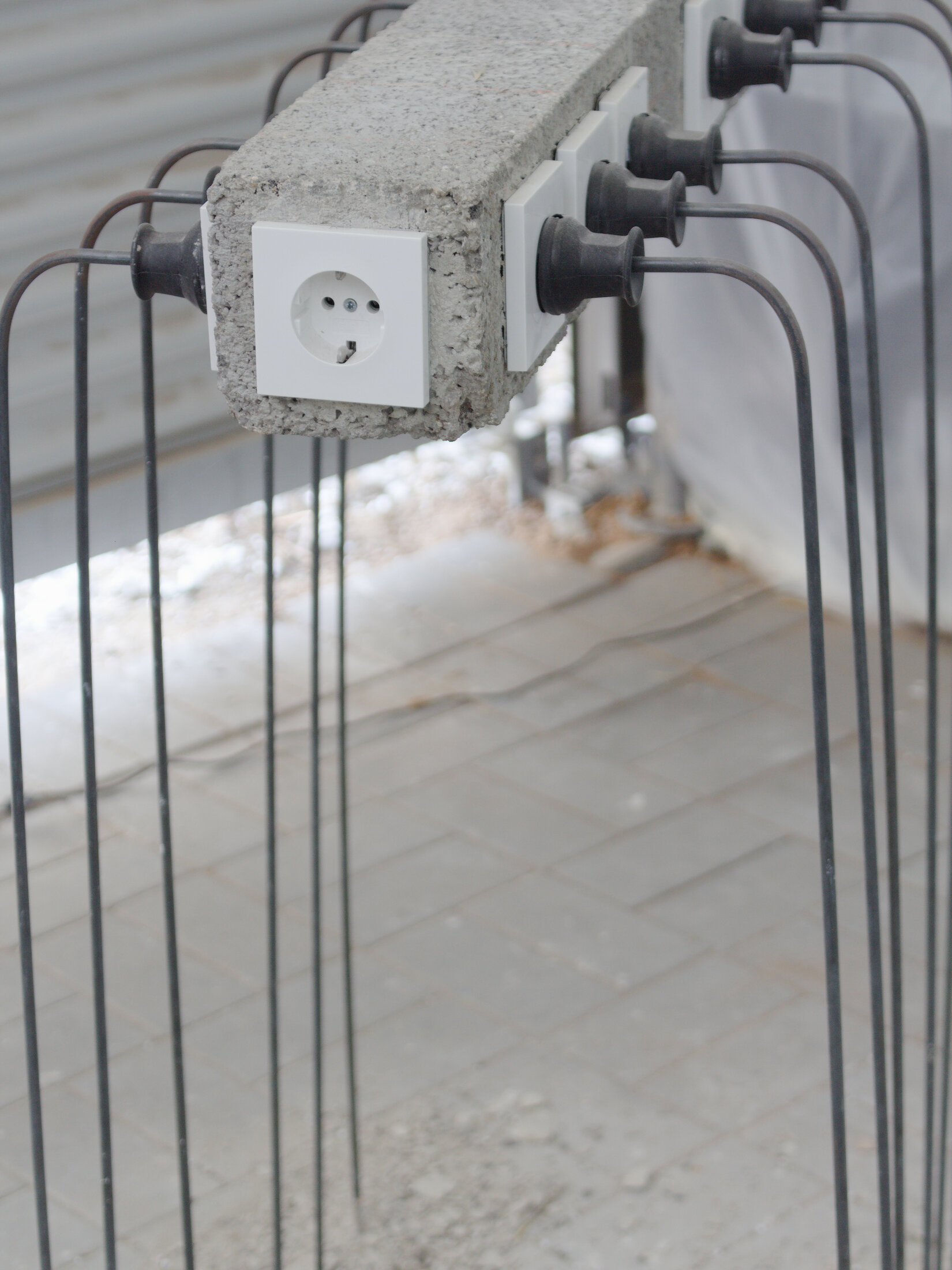 Provider, detail: a white socket set into a concrete beam, black plugs and steel rods hanging from it
