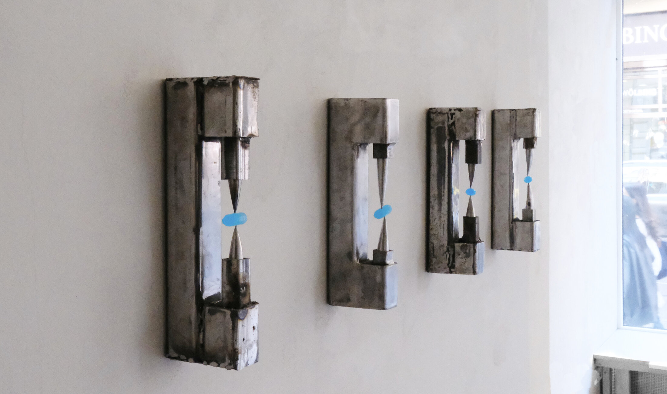 Dispenser: four welded sheet-metal wall objects of decreasing size, each holding blue candy