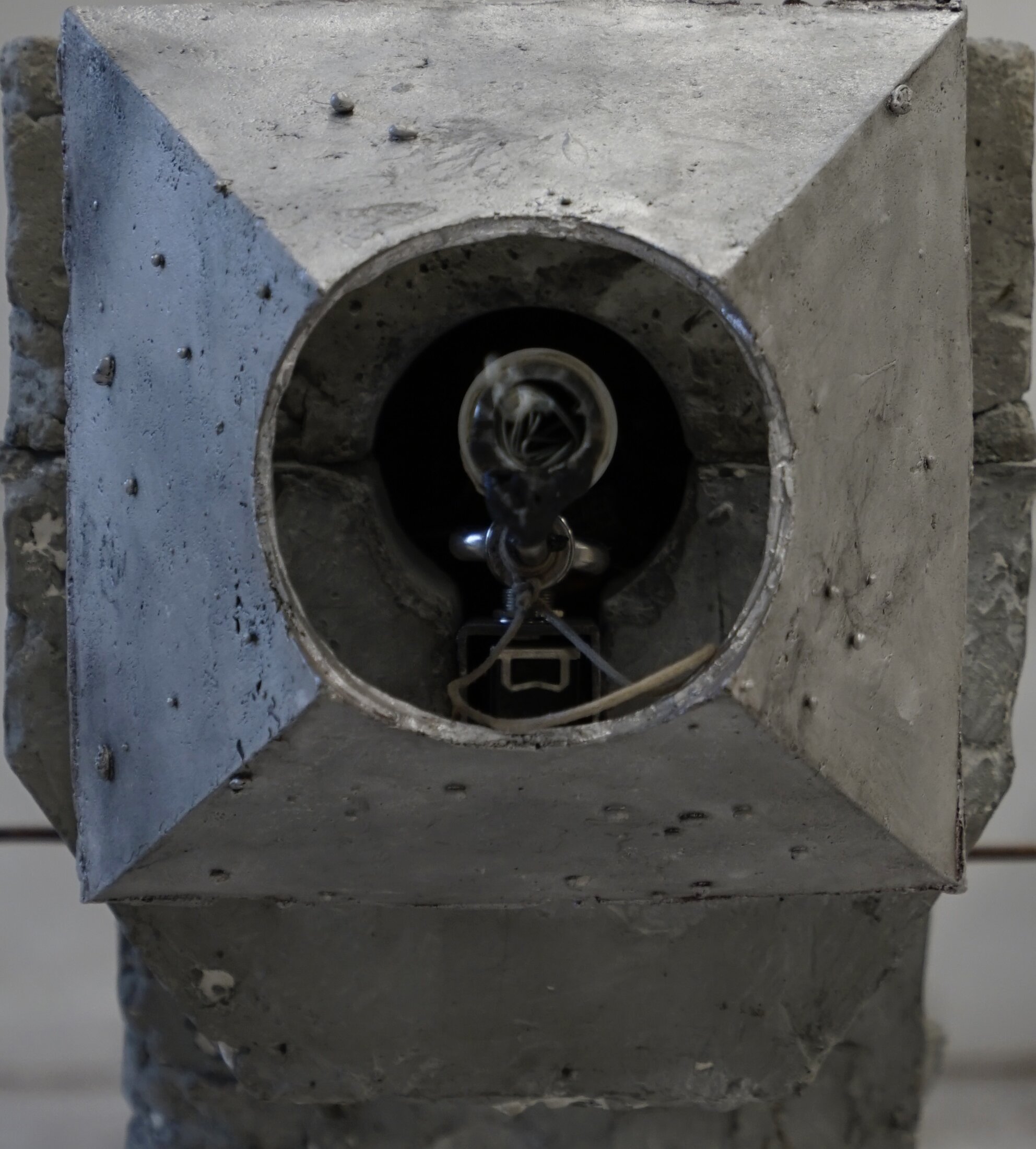 Visualizer, detail: a bare bulb inside the round opening of the faceted concrete head